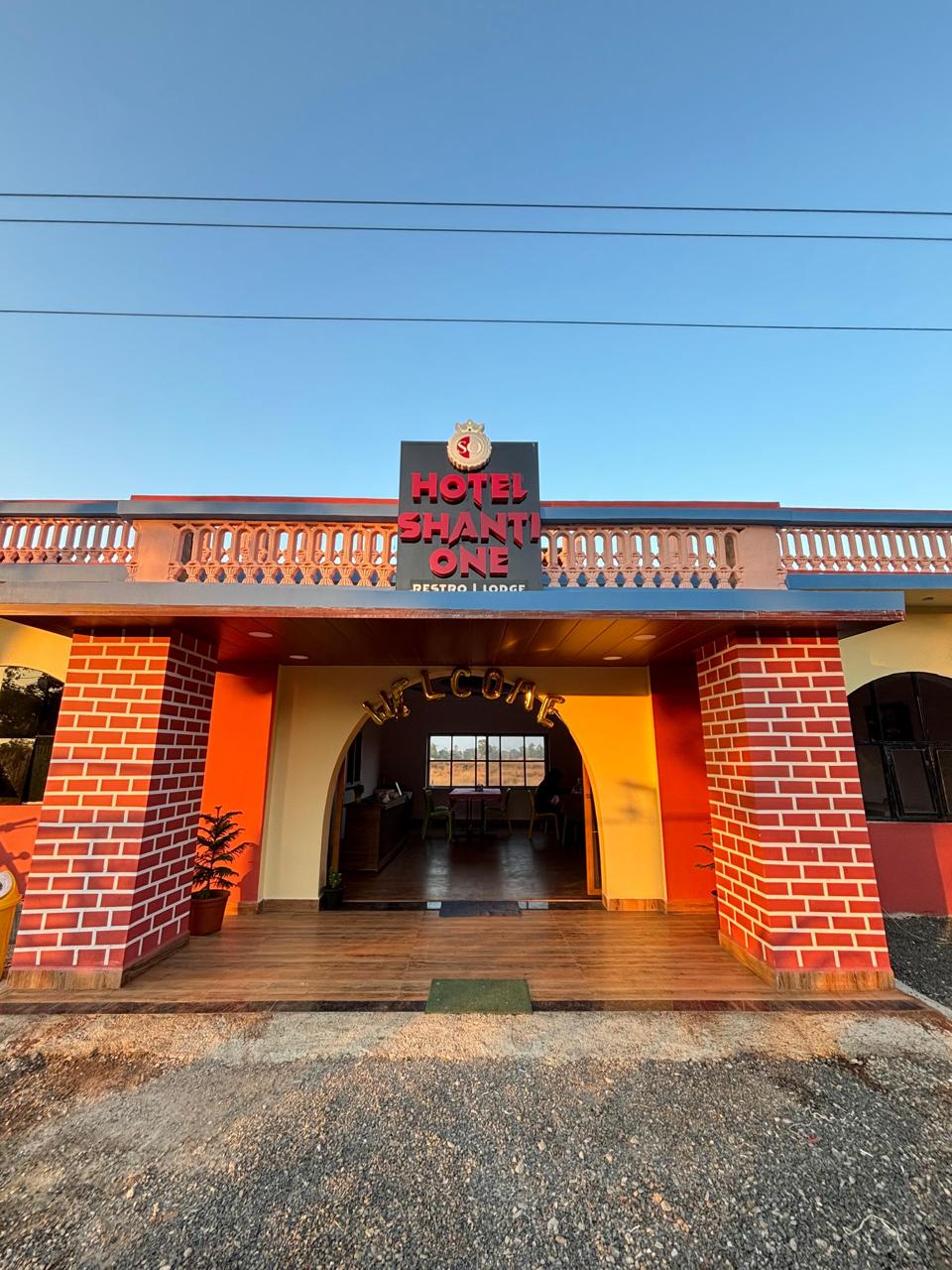 Front entrance of the hotel at golden hour — brick-clad pillars, a balustraded roofline and an arched “Welcome” doorway