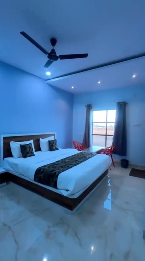 Spacious room with sky-blue walls, a double bed with a patterned runner, red chairs and a large window