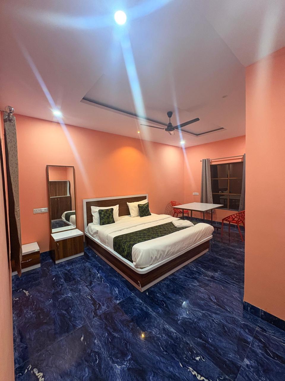 Guest room with coral walls, a double bed with white linen and green cushions, a full-length mirror and a deep-blue marble floor