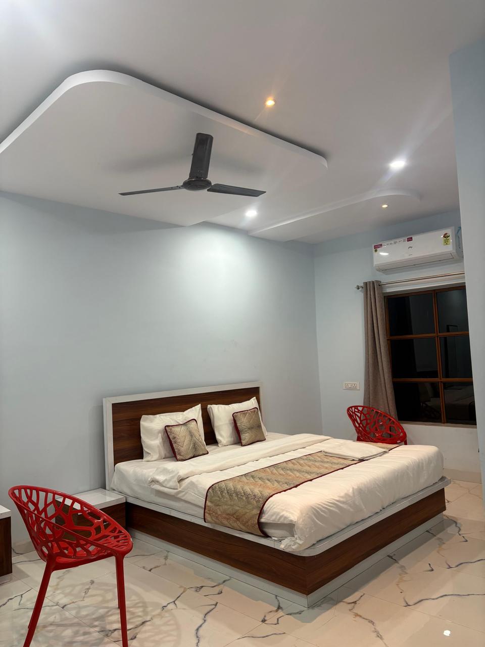 Bright guest room with pale grey-blue walls, a double bed, two red sculptural chairs and white marble flooring